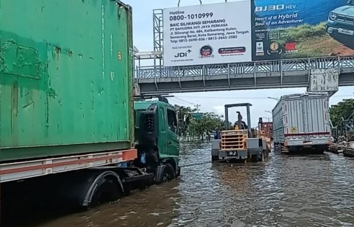 Alat berat dikerahkan untuk membantu truk yang terjebak banjir di jalur Pantura Demak. (Foto : Sam)