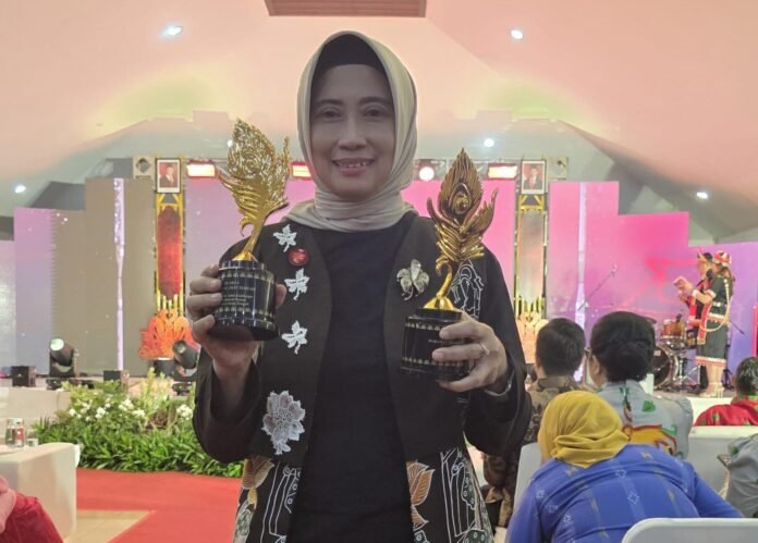 Kepala Dinas Pariwisata Kabupaten Demak memperlihatkan dua trofi Juara 1 API Award 2025 yang berhasil diraih Demak untuk kategori Makanan Tradisional dan Kampung Adat. (Foto:Sam)