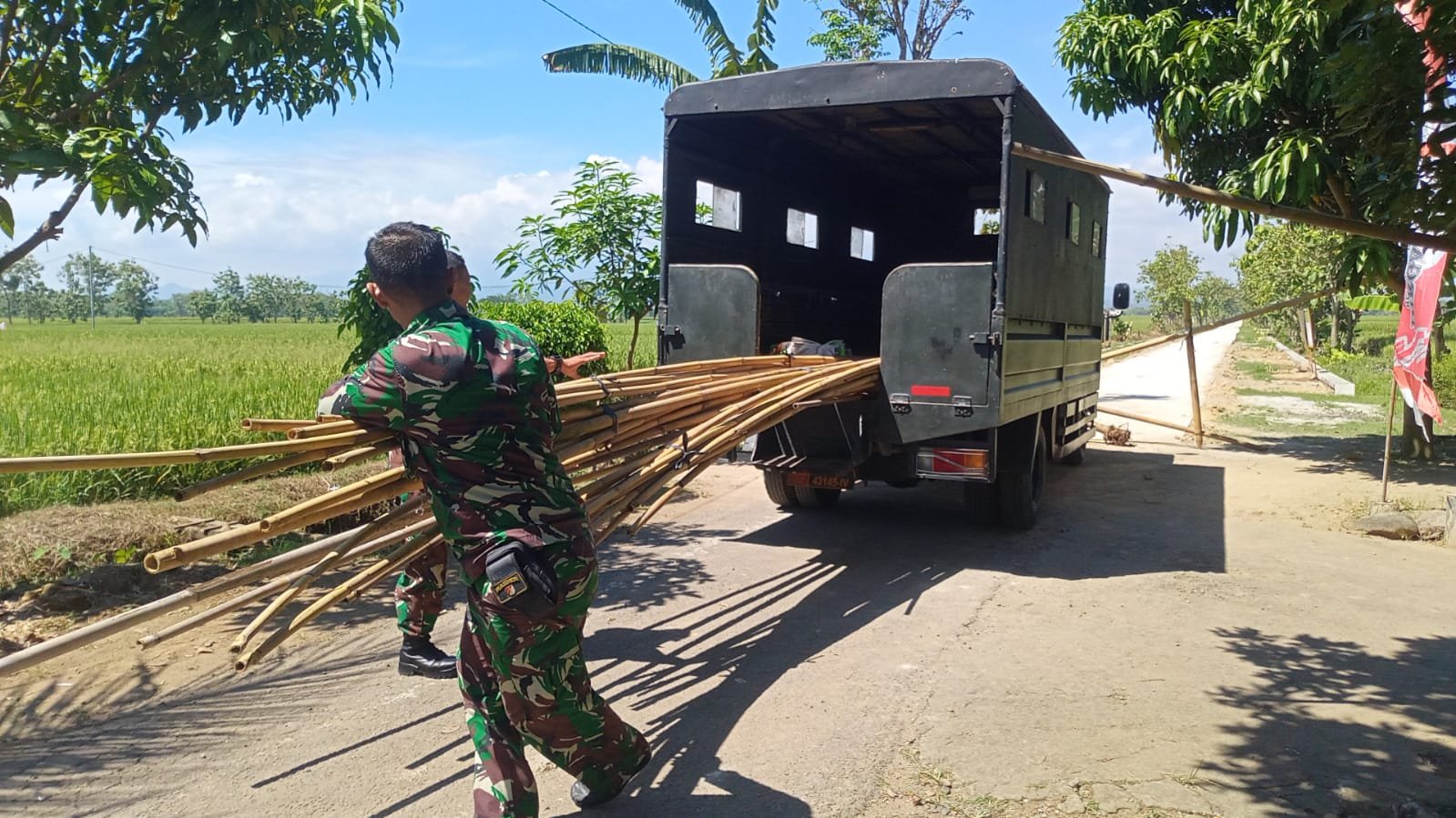 TMMD Sragen Ketua Kelompok Tata Usaha dan Urusan Dalam (Kapok Tuud) Serma Ngatiman bersama anggota Satgas lainnya tampak sibuk mendroping bambu untuk persiapan pemasangan umbul-umbul penutupan TMMD. (Foto : Dok TMMD Sragen)